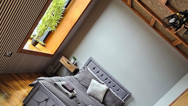 A modern bedroom with a loft bed, wooden flooring, a small window with a plant, and a built-in bench. - The Shepherds Rest (Sowerby Bridge)