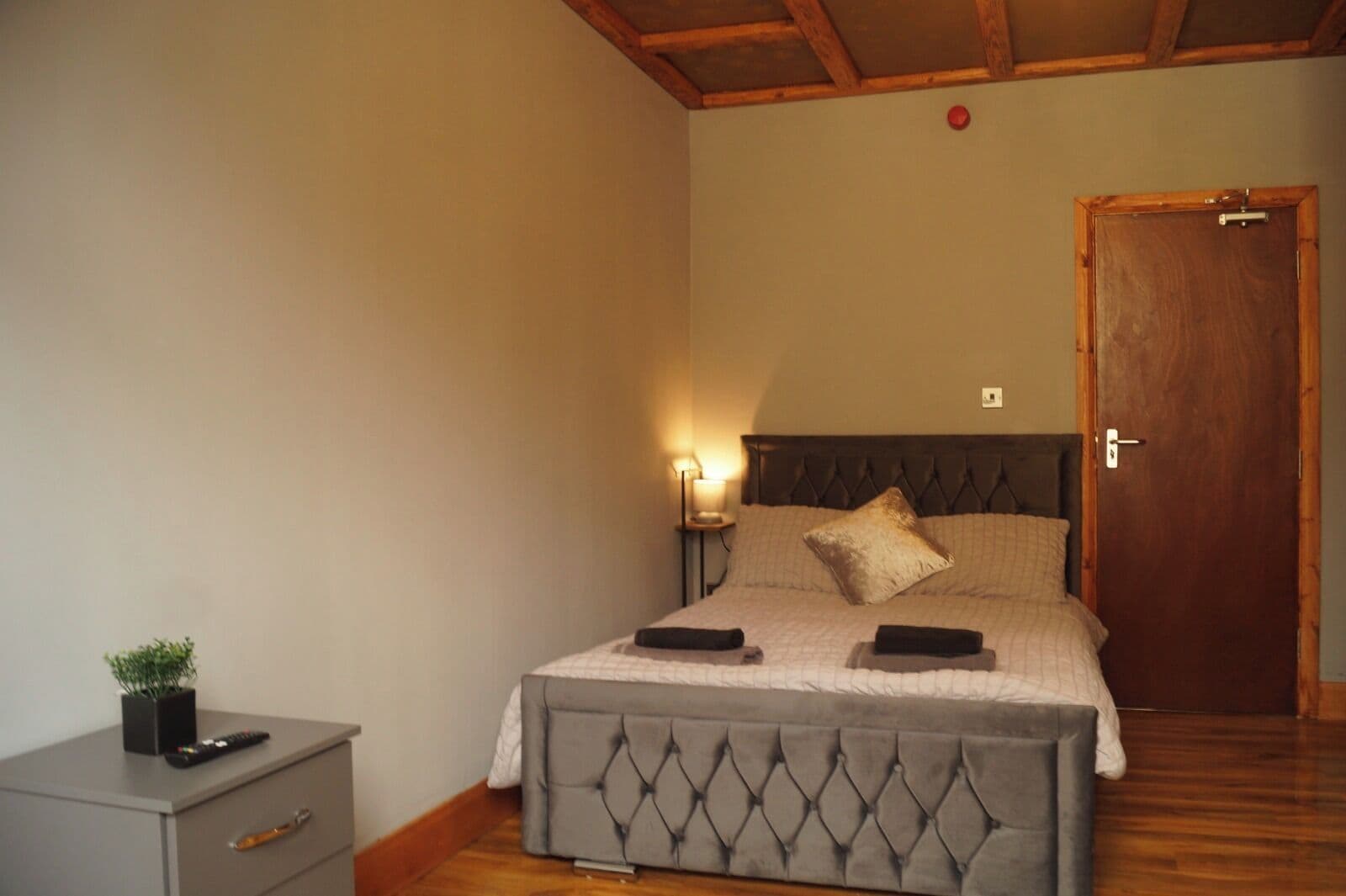 A bedroom with a bed, bedside table, lamp, and a door.