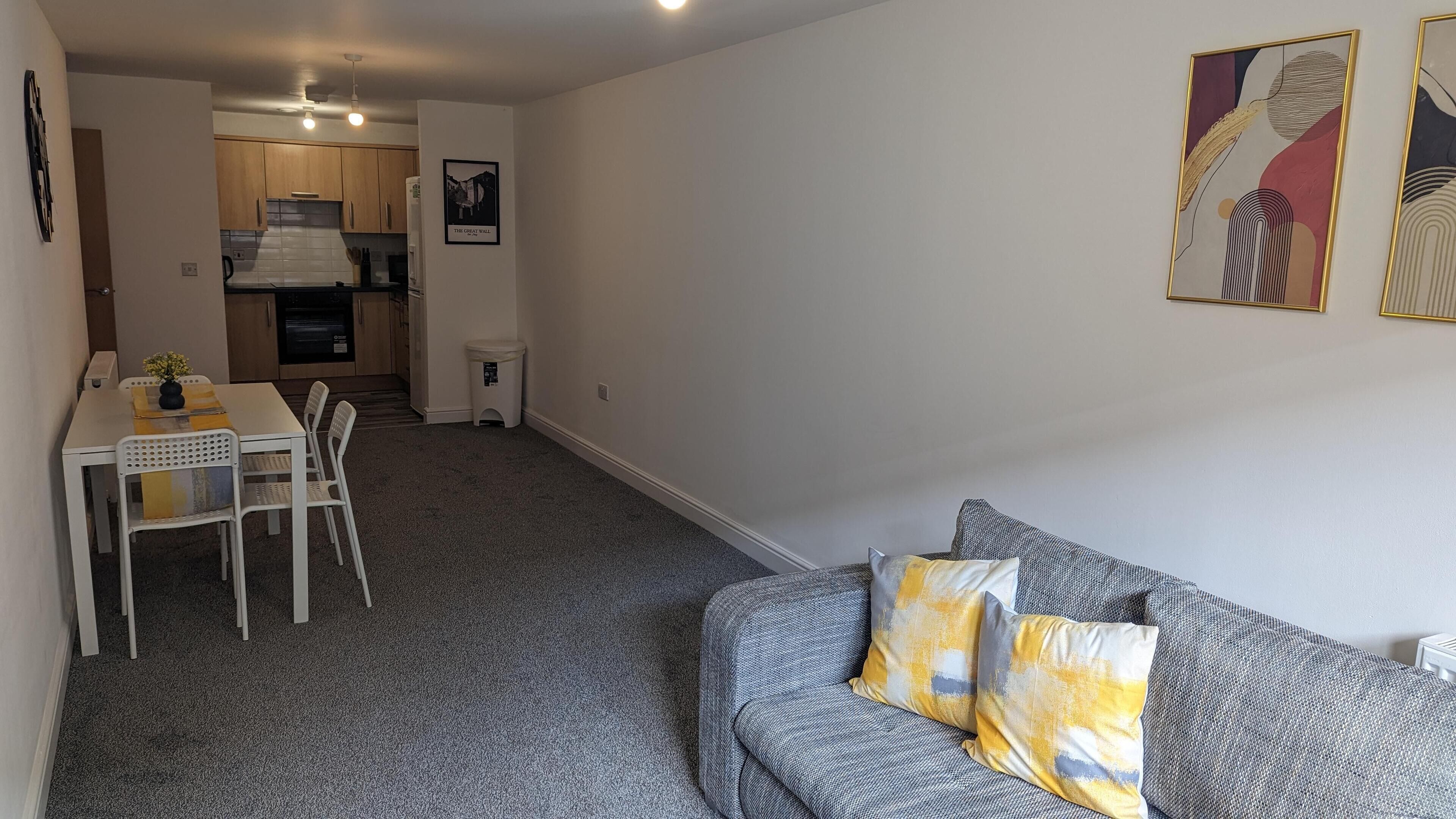 A compact living space with a dining area, kitchenette, and a grey sofa with yellow cushions.