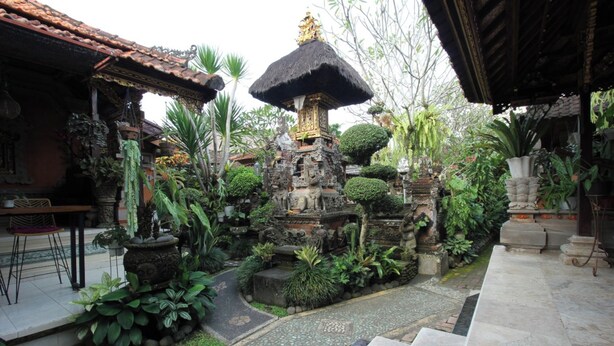 A courtyard with a stone structure, potted plants, and a tiled pathway. - Capital O 94011 Binhari Guest House (Ubud)