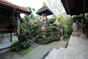 A courtyard with a stone structure, potted plants, and a tiled pathway.