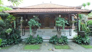 A traditional building with a tiled roof, a central entrance, and a garden with various plants and a tiled pathway. - Capital O 94011 Binhari Guest House (Ubud)