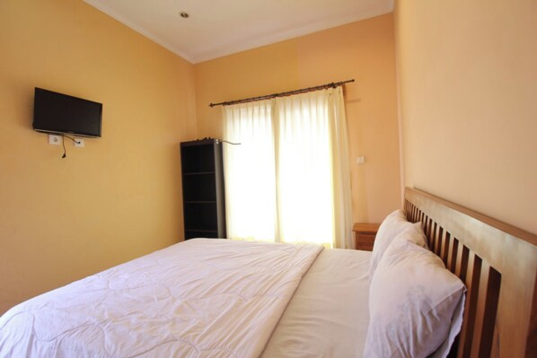 A bedroom with a bed, a television mounted on the wall, and a window with curtains.