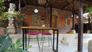 A traditional Balinese pavilion with ornate carvings, a wooden table with two chairs, and potted plants. - Capital O 94011 Binhari Guest House (Ubud)