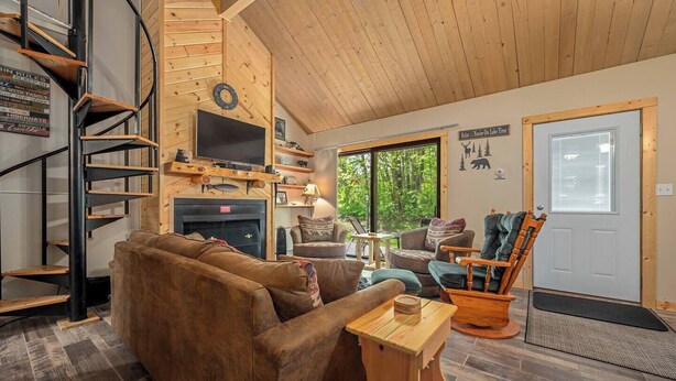 Un salón acogedor con chimenea, televisor montado en la pared, sofá confortable, una silla de madera y una escalera.