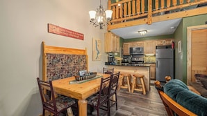 Una cocina acogedora con armarios de madera, una mesa de comedor con sillas, una lámpara de araña y una escalera de madera que sube a la zona superior.