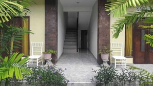 A covered walkway with potted plants and white chairs, leading to a staircase. - OYO 94014 The Sanya Homestay (Mengwi)