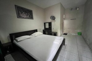 A bedroom with a bed, a nightstand, a dresser, a mirror, a wall-mounted fan, and a door. - OYO 94014 The Sanya Homestay (Mengwi)