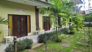 A building with two doors, each marked with a number. There are chairs and a small garden area with plants and a pathway. - OYO 94014 The Sanya Homestay (Mengwi)