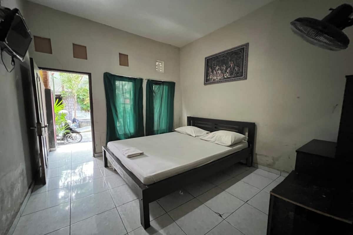 A bedroom with a bed, curtains, a fan, a picture on the wall, and a door leading to a balcony.