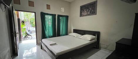 A bedroom with a bed, curtains, a fan, a picture on the wall, and a door leading to a balcony.