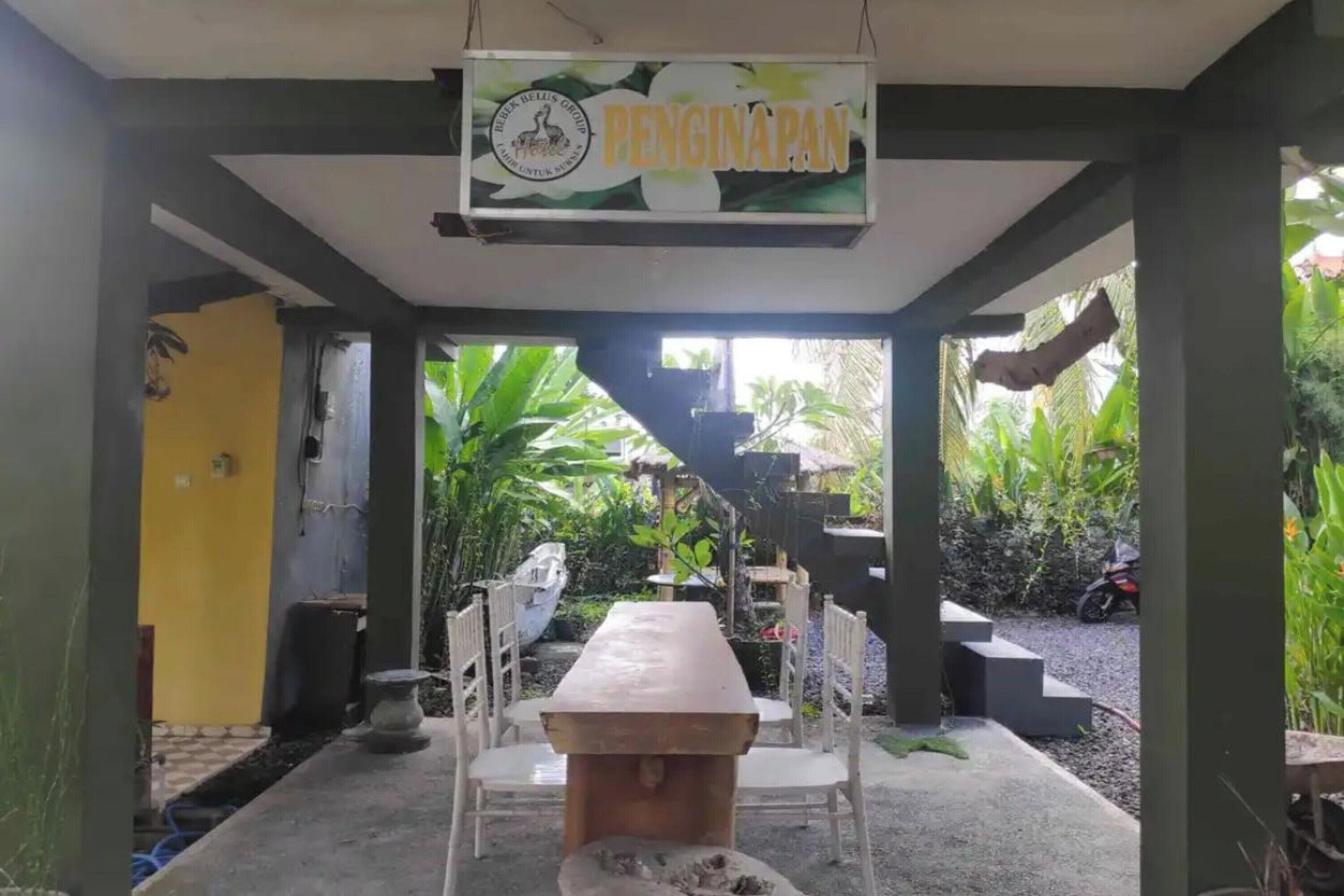 A covered outdoor seating area with a table and chairs, surrounded by greenery and a sign reading "PENGINAPAN".