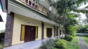 A building with numbered doors, a balcony, and a well-maintained garden with various plants. - OYO 94014 The Sanya Homestay (Mengwi)