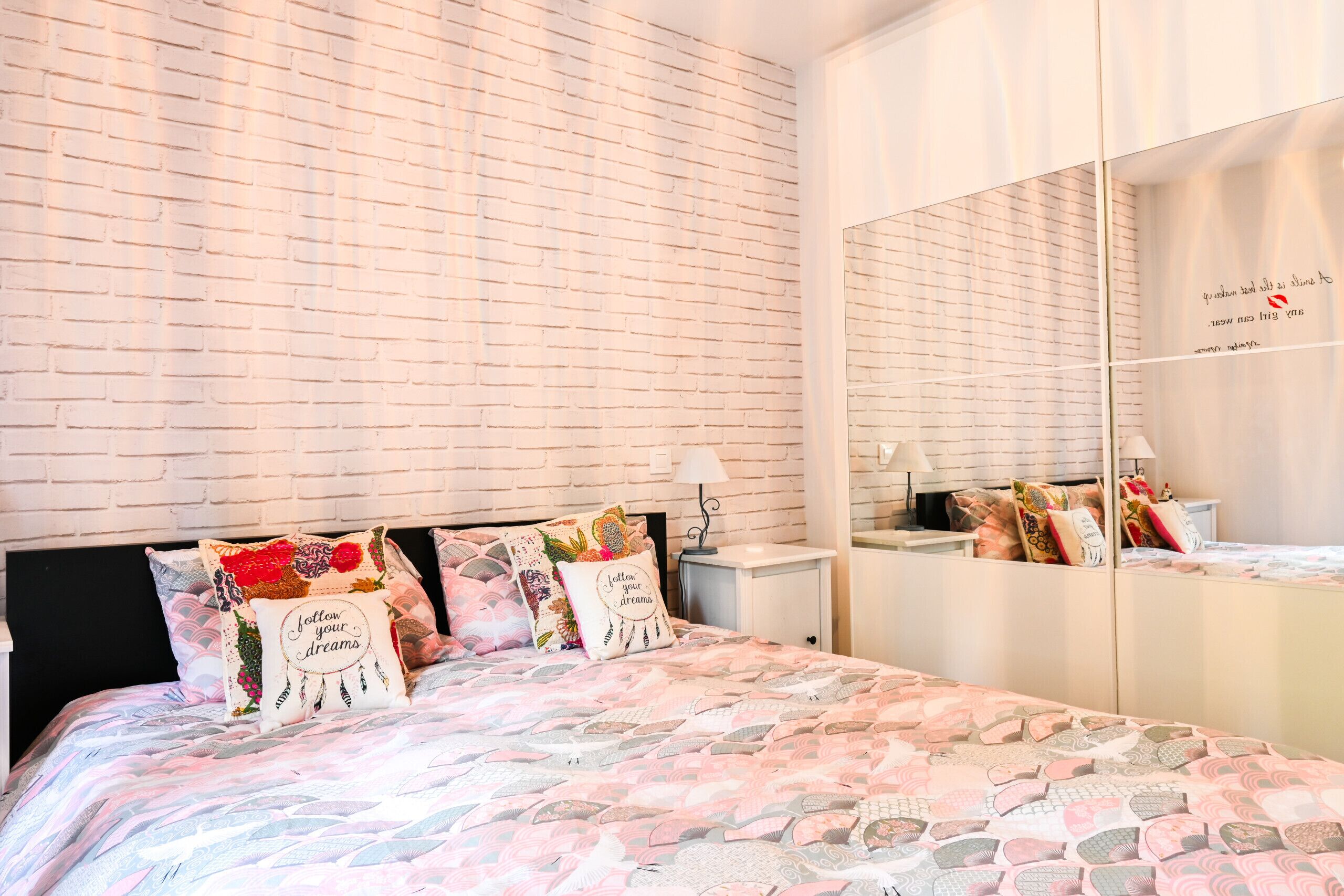 Un dormitorio con pared de ladrillos, cama con ropa de cama estampada y espejo con marco decorativo.