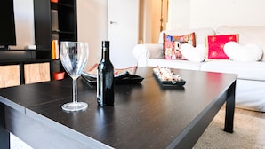 Un salon moderne avec une table basse en bois foncé, un verre à vin et une bouteille. Un canapé blanc avec des coussins colorés se trouve à l’arrière-plan.