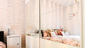 Une chambre moderne avec un mur au motif de briques, une armoire à miroir, un lit avec une literie colorée et des lampes de chevet.