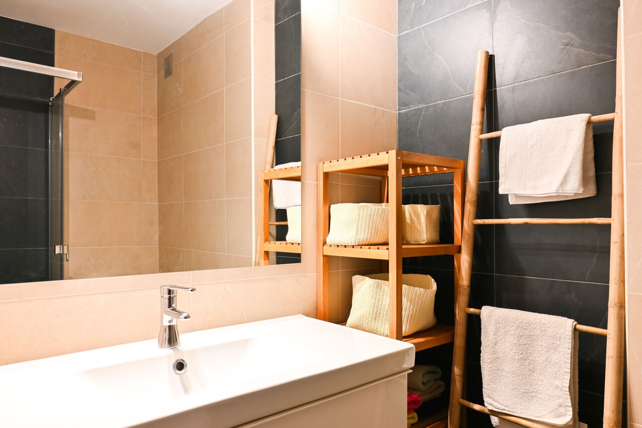 Un baño con lavamanos blanco, espejo y toallero de madera con toallas.