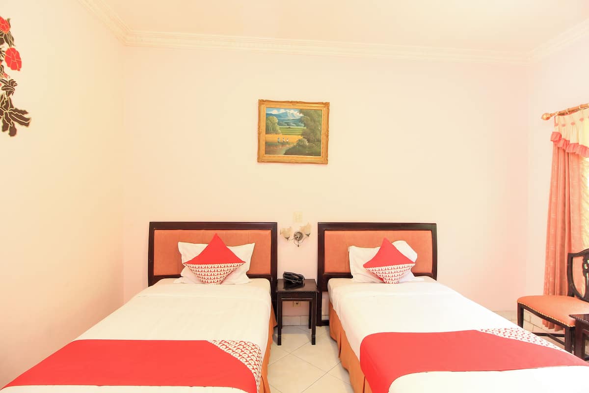 A hotel room with two beds, a nightstand, a chair, a painting on the wall, and a window with curtains.