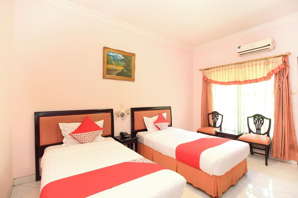 A hotel room with two beds, a painting on the wall, an air conditioner, and a window with curtains.