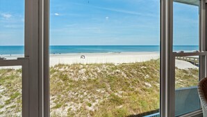 Vista dalla finestra su una spiaggia con un paesaggio sabbioso e cielo sereno.