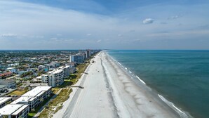 Paesaggio costiero con una lunga spiaggia, edifici lungo la riva e un molo che si protende nell'acqua.