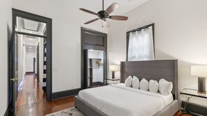A bedroom with a large bed, a ceiling fan, a nightstand with a lamp, and a mirror on the wall. - Updated Bywater Apt 5 minutes to French Quarter (New Orleans)