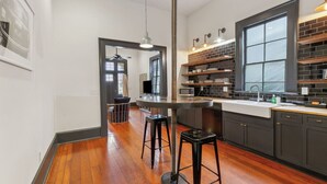 A modern kitchen with dark cabinetry, a large window, and a bar area with stools. - Updated Bywater Apt 5 minutes to French Quarter (New Orleans)