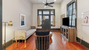 A modern living room with a sofa, a small round table, a television, and a ceiling fan. - Updated Bywater Apt 5 minutes to French Quarter (New Orleans)