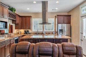 A kitchen with a central island, stainless steel appliances, and brown leather chairs.