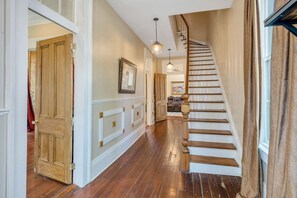 A wooden staircase with a handrail, a hallway with a white door, and a hanging light fixture.