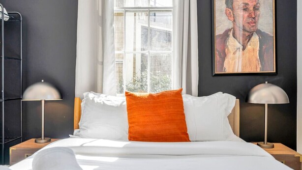 Een hotelkamer met een bed, twee bedlampen, een raam met gordijnen en een schilderij aan de muur.