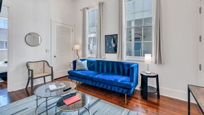 Een moderne woonkamer met een blauwe bank, een ronde spiegel, een klein rond tafeltje en een stoel.