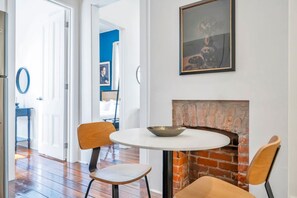 A dining area with a round table, two chairs, a brick fireplace, and a framed picture on the wall.
