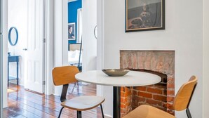 Een eetgedeelte met een ronde tafel, twee stoelen, een metselstenen openhaard en een ingelijst kunstwerk aan de wand.