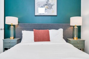 A neatly made bed with white linens and a red accent pillow, flanked by two bedside tables with lamps. - Hip & Stylish Magazine St. Apt | Balcony & Parking (New Orleans)