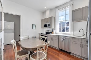 A modern kitchen with white cabinets, a stainless steel refrigerator, and a dining table with chairs. - Hip & Stylish Magazine St. Apt | Balcony & Parking (New Orleans)