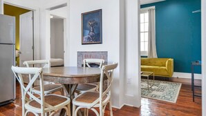 A dining area with a round table and four chairs, a painting on the wall, a yellow sofa, and a teal wall in the background.