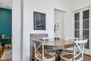 A dining area with a round table, white chairs, and a painting above. - Hip & Stylish Magazine St. Apt | Balcony & Parking (New Orleans)