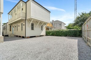 A two-story building with a balcony, a gravel driveway, and a hedge in the background. - Hip & Stylish Magazine St. Apt | Balcony & Parking (New Orleans)