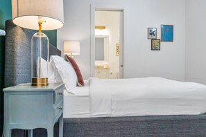 A hotel room with a bed, a nightstand, a lamp, and a door leading to a bathroom. - Hip & Stylish Magazine St. Apt | Balcony & Parking (New Orleans)