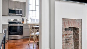 A kitchen with stainless steel appliances, a dining area with a white table and chairs, and a brick fireplace.