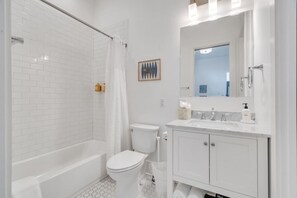 A modern bathroom with white tiles, a bathtub, a toilet, and a vanity with a mirror. - Hip & Stylish Magazine St. Apt | Balcony & Parking (New Orleans)