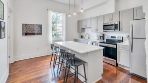 A modern kitchen with white cabinets, stainless steel appliances, and a large island with bar stools. - Chic Magazine St. Apt | King Bed, Balcony, Parking (New Orleans)