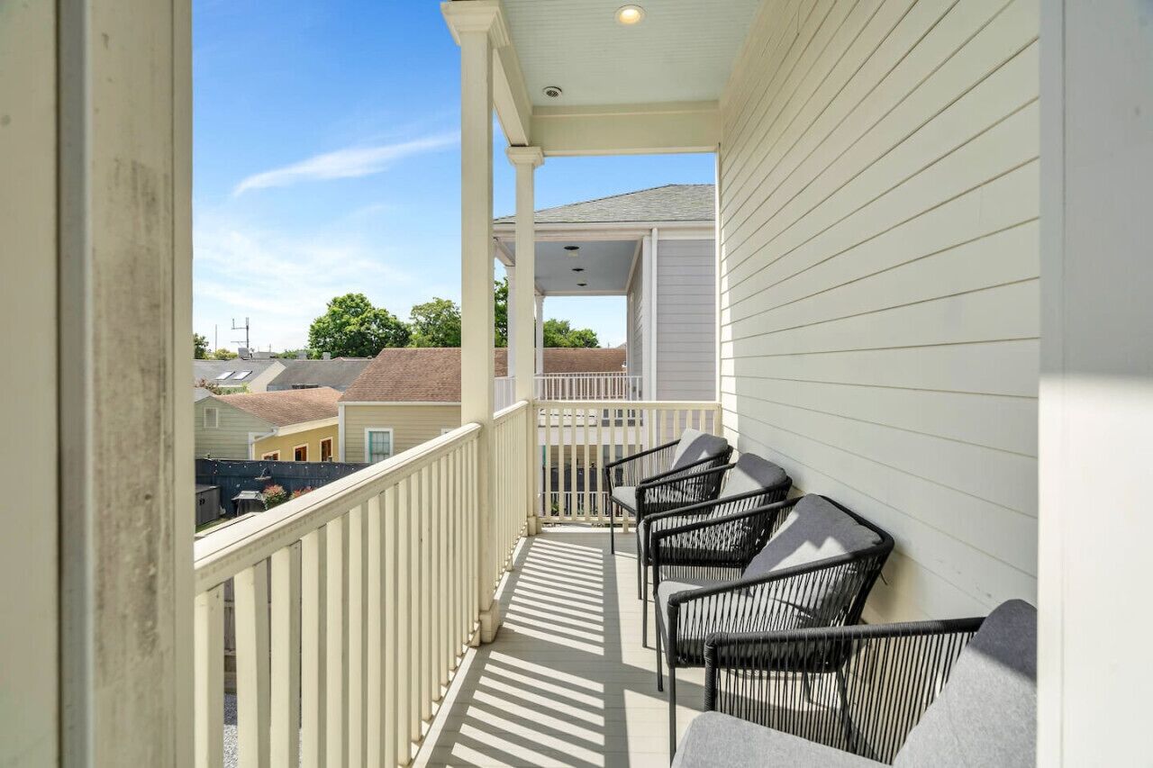 Un balcon doté de balustrades blanches et d’un espace abrité, comprenant quatre chaises noires et une table.
