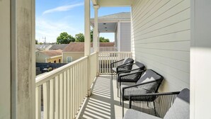 A balcony with white railings and a covered area, featuring four black chairs and a table. - Chic Magazine St. Apt | King Bed, Balcony, Parking (New Orleans)