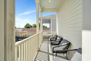Un balcon doté de balustrades blanches et d’un espace abrité, comprenant quatre chaises noires et une table.