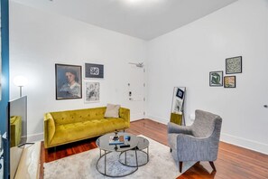 Un salon moderne avec un canapé jaune, un fauteuil gris, une table basse et des œuvres d’art accrochées aux murs.