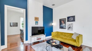 Un salon moderne avec un canapé jaune, un téléviseur à écran plat et des œuvres d’art accrochées aux murs.