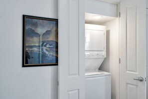 A laundry room with a washing machine and dryer, a framed painting on the wall, and a white door.