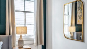 Une pièce avec une fenêtre, une lampe sur une table d’appoint et un miroir fixé au mur.